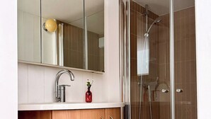 Ein modernes Badezimmer mit einem hölzernen Waschtisch, einem großen Spiegel, einer Dusche mit Glastür und einem punktierten Boden.
