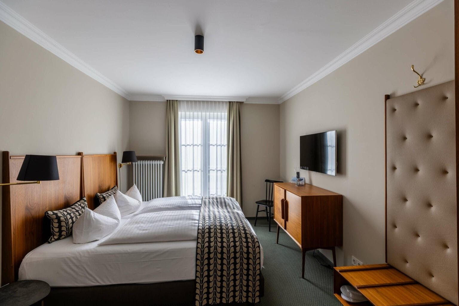 Habitación de hotel con una cama grande, un escritorio, un televisor y una ventana con cortinas.