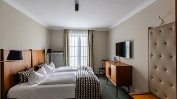 Habitación de hotel con una cama grande, un escritorio, un televisor y una ventana con cortinas.