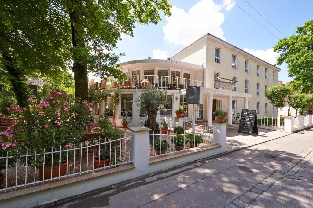 Un hotel amb una façana corba, nombroses balcons i una zona de jardí amb plantes en testos.