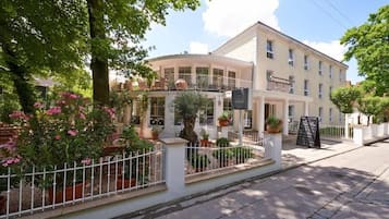 Un hotel amb una façana corba, nombroses balcons i una zona de jardí amb plantes en testos.