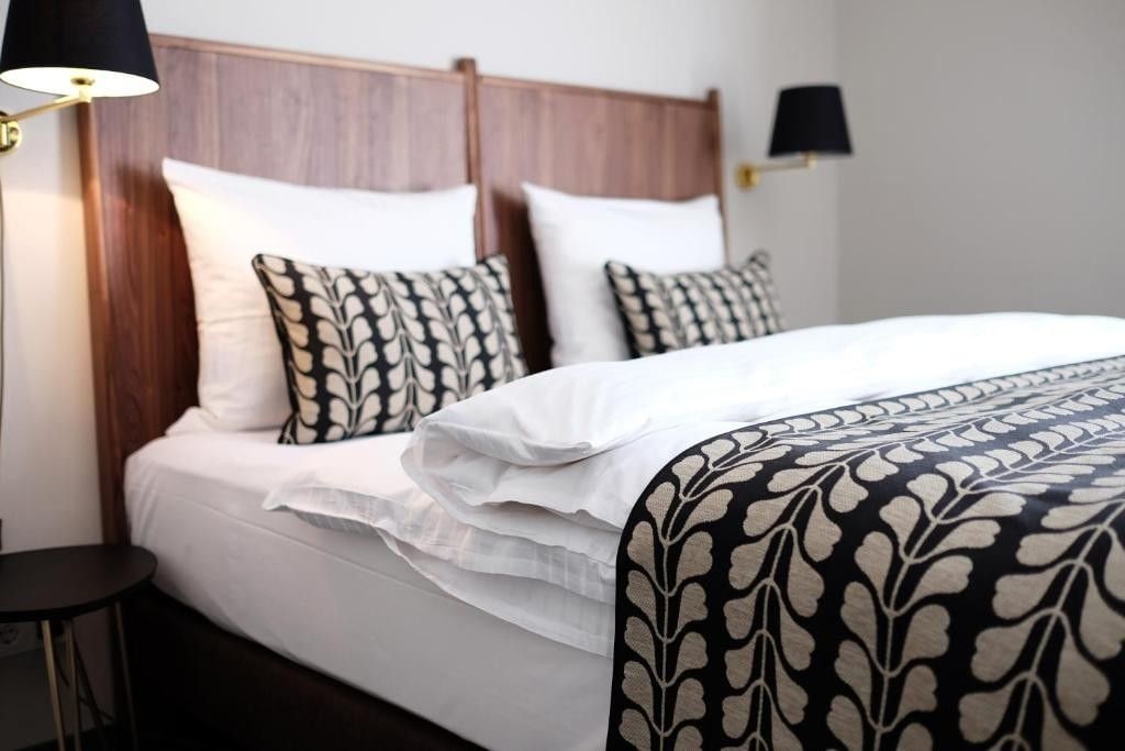 A neatly made bed with white linens and patterned pillows, a bedside lamp, and a small table.