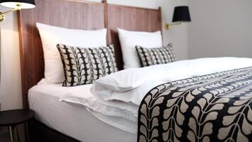 A neatly made bed with white linens and patterned pillows, a bedside lamp, and a small table.