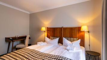 A hotel room with a large bed, two bedside lamps, a desk, and a chair.