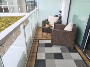 A balcony with a checkered floor mat, wicker furniture, and a small table with a plant. - A fully furnished apartment just 5 minutes from a wide, sandy beach. (Kołobrzeg)