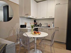 A modern kitchen with a round dining table, clear chairs, and a vase of flowers. - A fully furnished apartment just 5 minutes from a wide, sandy beach. (Kołobrzeg)
