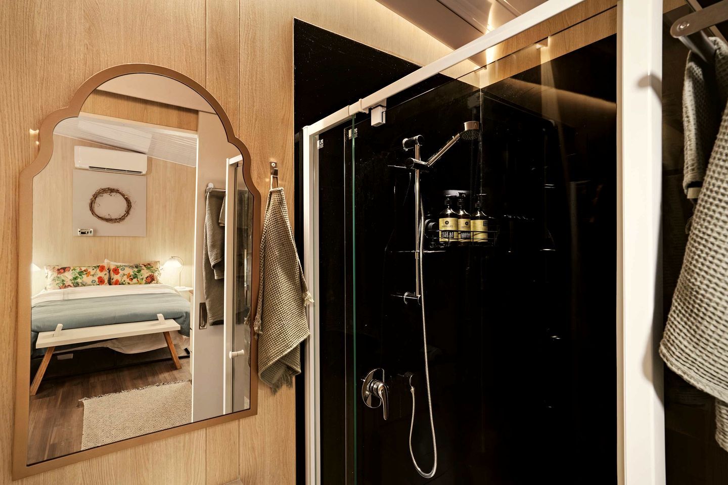 Un baño moderno con cabina de ducha de vidrio, un espejo y una cama con edredón estampado con motivos florales.
