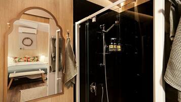 Un baño moderno con cabina de ducha de vidrio, un espejo y una cama con edredón estampado con motivos florales.