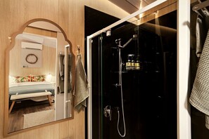 A modern bathroom with a glass shower enclosure, a mirror, and a bed with a floral bedspread.