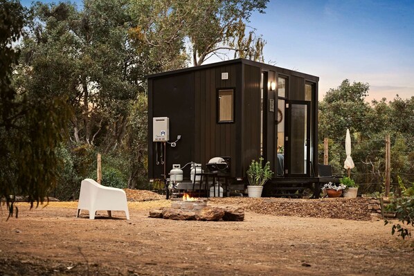 A compact cabin with a small porch, a fire pit, and outdoor seating.