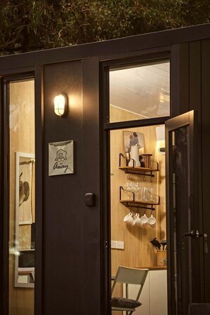 A room with a wooden door, a wall-mounted light, a sign, and a shelf with cups and a vase.