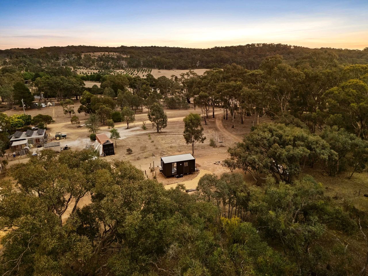A rural landscape with a small cabin surrounded by trees and open fields.