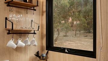 Une cuisine compacte dotée d’un évier intégré, d’une fenêtre donnant sur les arbres et d’une étagère où sont rangées des tasses et des verres.