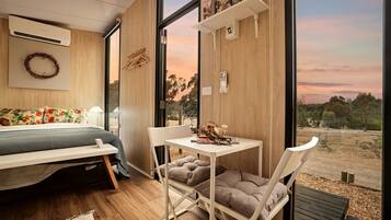 Une chambre moderne avec un lit, une petite table et une chaise. Une grande fenêtre offre une vue sur l’extérieur.