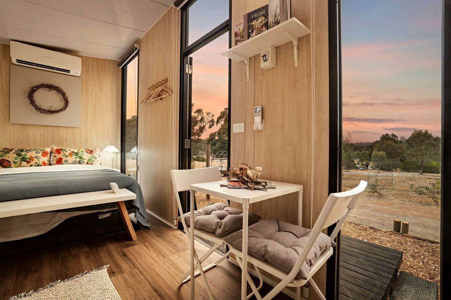 Een moderne slaapkamer met een bed, een klein tafeltje en een stoel. Een groot raam biedt uitzicht op het omliggende landschap.