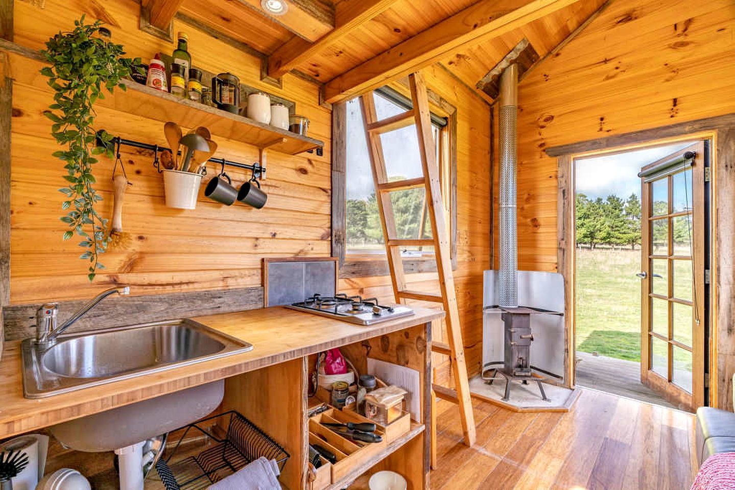 A wooden cabin kitchen with a large sink, stove, and open shelving.