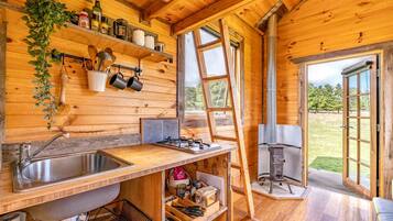 A wooden cabin kitchen with a large sink, stove, and open shelving.