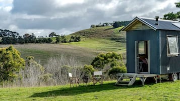 Une petite cabane à un seul étage, avec un toit en métal, située sur un champ herbeux, d’où l’on peut admirer des collines ondoyantes à l’horizon.