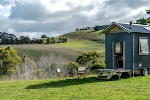 Une petite cabane à un seul étage, avec un toit en métal, située sur un champ herbeux, d’où l’on peut admirer des collines ondoyantes à l’horizon.