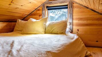 A wooden cabin bedroom with a bed, pillows, and a window.