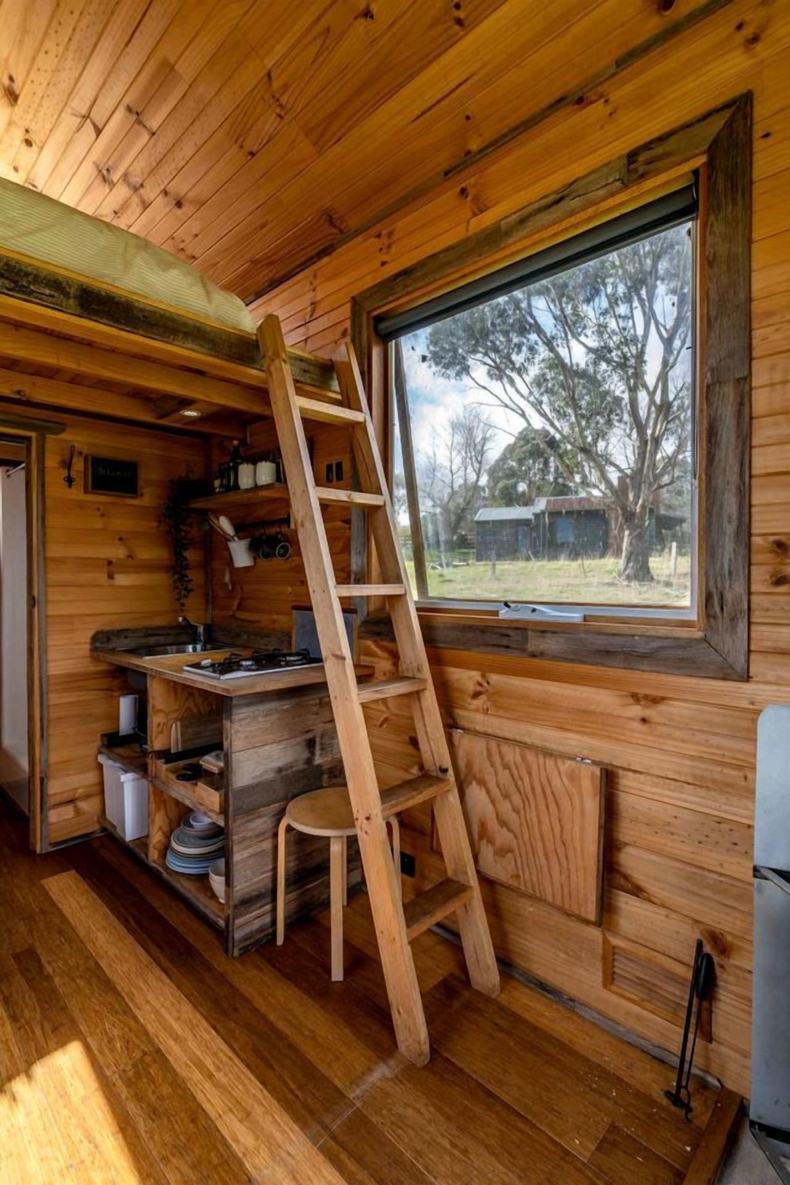 A wooden interior with a kitchen area, a window, and a ladder.