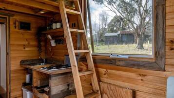 A wooden interior with a kitchen area, a window, and a ladder.