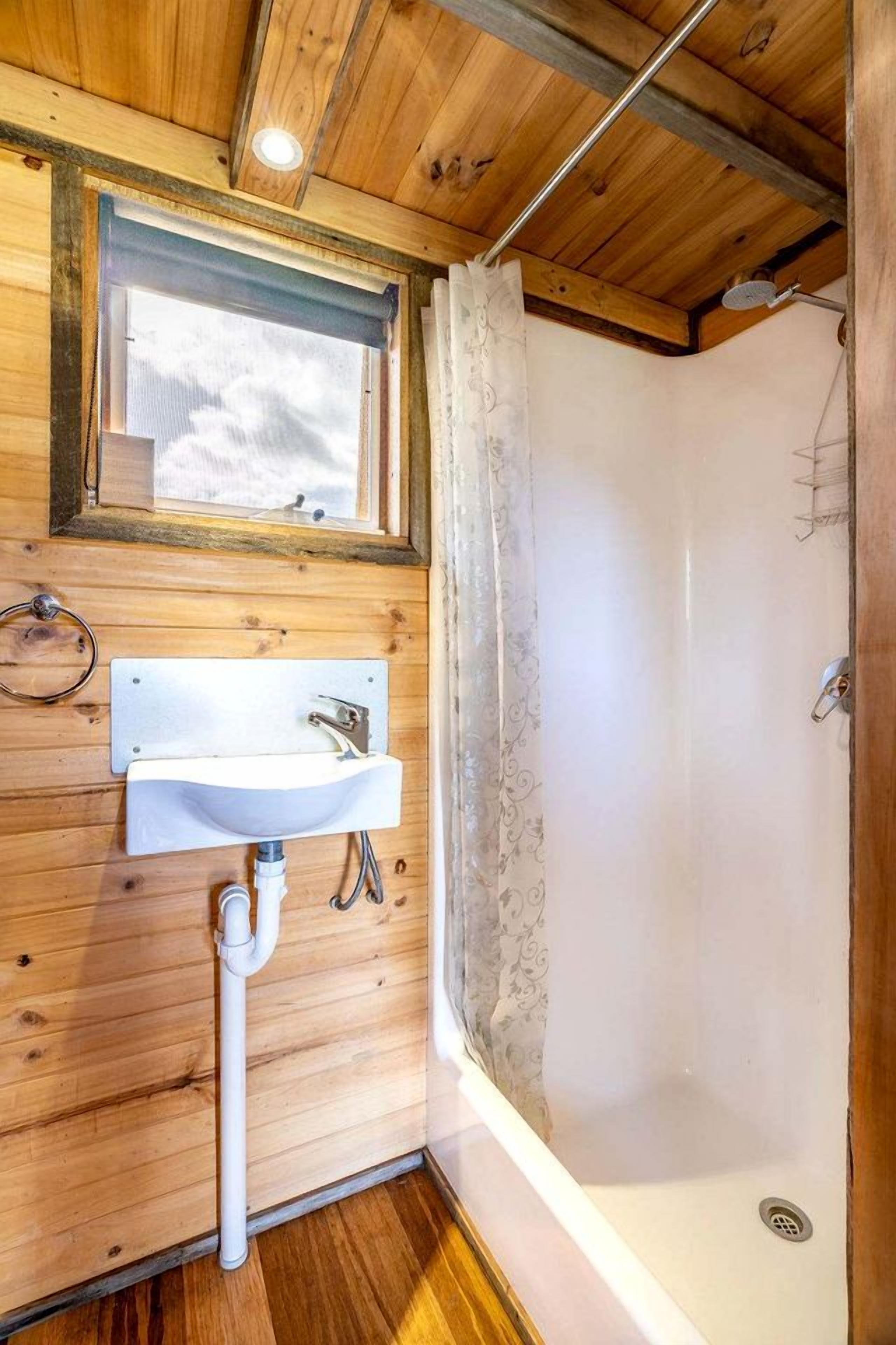A wooden interior with a white sink, a shower, and a window with a view.