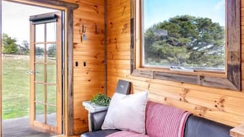 A wooden interior with a leather sofa, a window with a view, and a door leading outside.