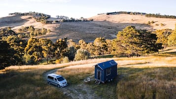 Un fourgon est garé dans un champ herbeux, avec une petite cabane bleue en premier plan.