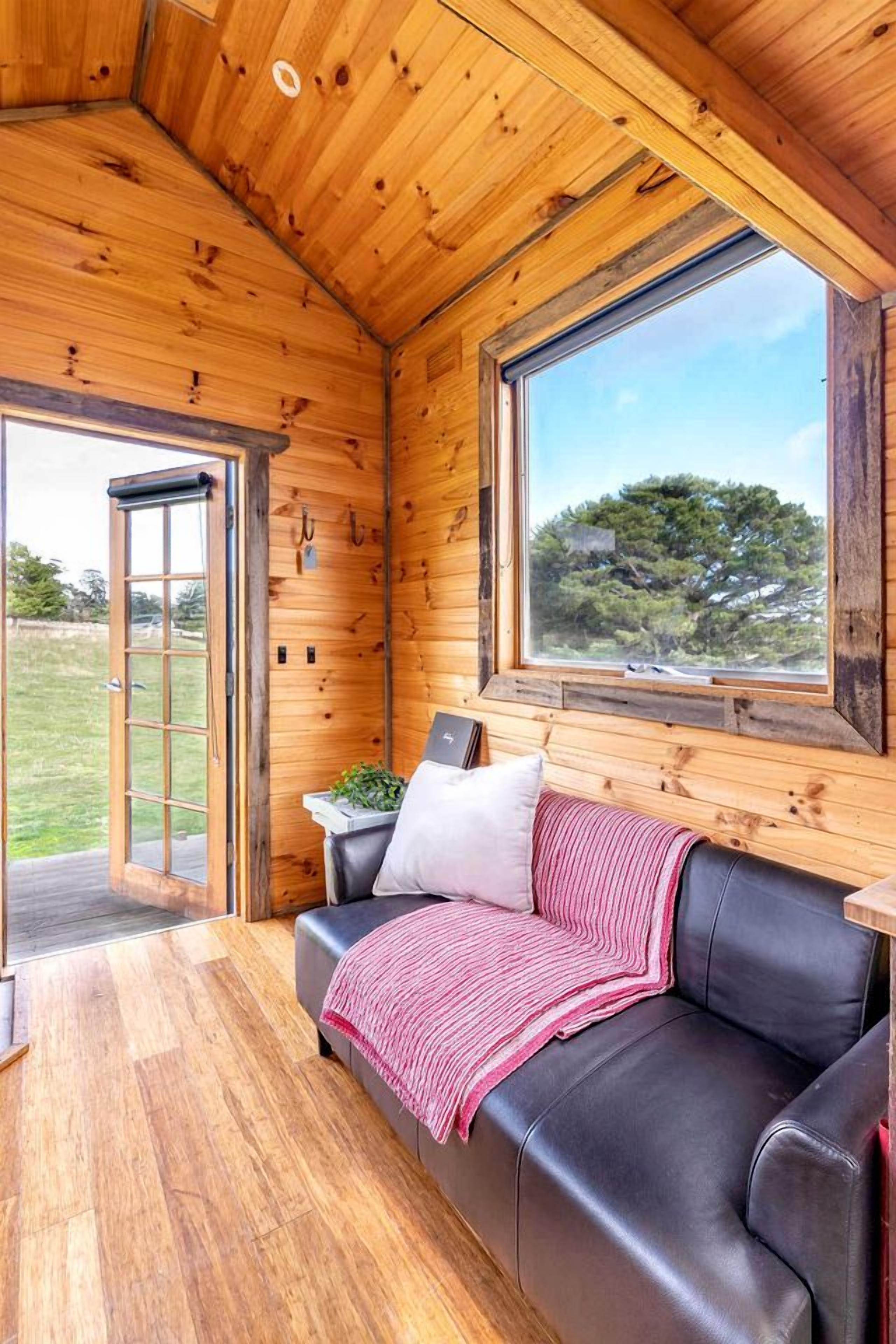 A wooden interior with a leather sofa, a window with a view, and a door leading outside.