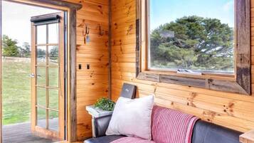 A wooden interior with a leather sofa, a window with a view, and a door leading outside.