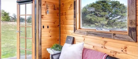 A wooden interior with a leather sofa, a window with a view, and a door leading outside.
