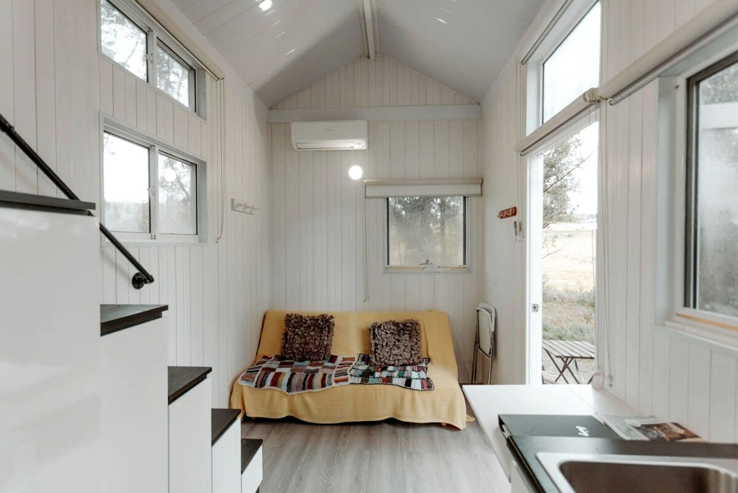 A compact room with a bed, a small table, a window, and a built-in air conditioning unit.