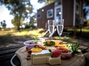 A wooden board with various cheeses, fruits, and a glass of wine on an outdoor table.