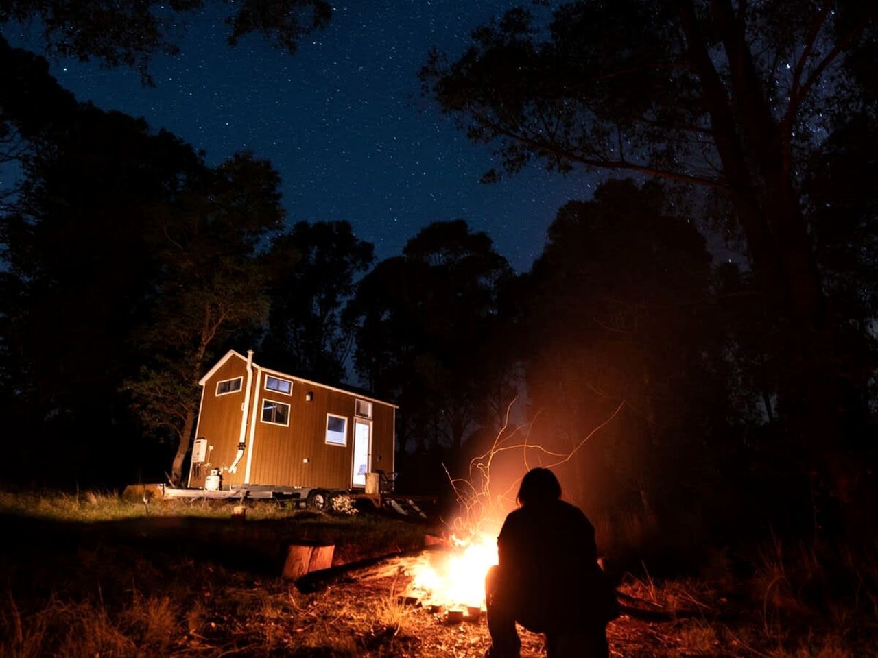 Eine Hütte mit kleiner Veranda, Feuerstelle und sternenklarer Nacht.