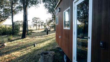 Une petite cabane en bois avec une porte en verre, située dans une zone herbeuse, avec des arbres en arrière-plan.