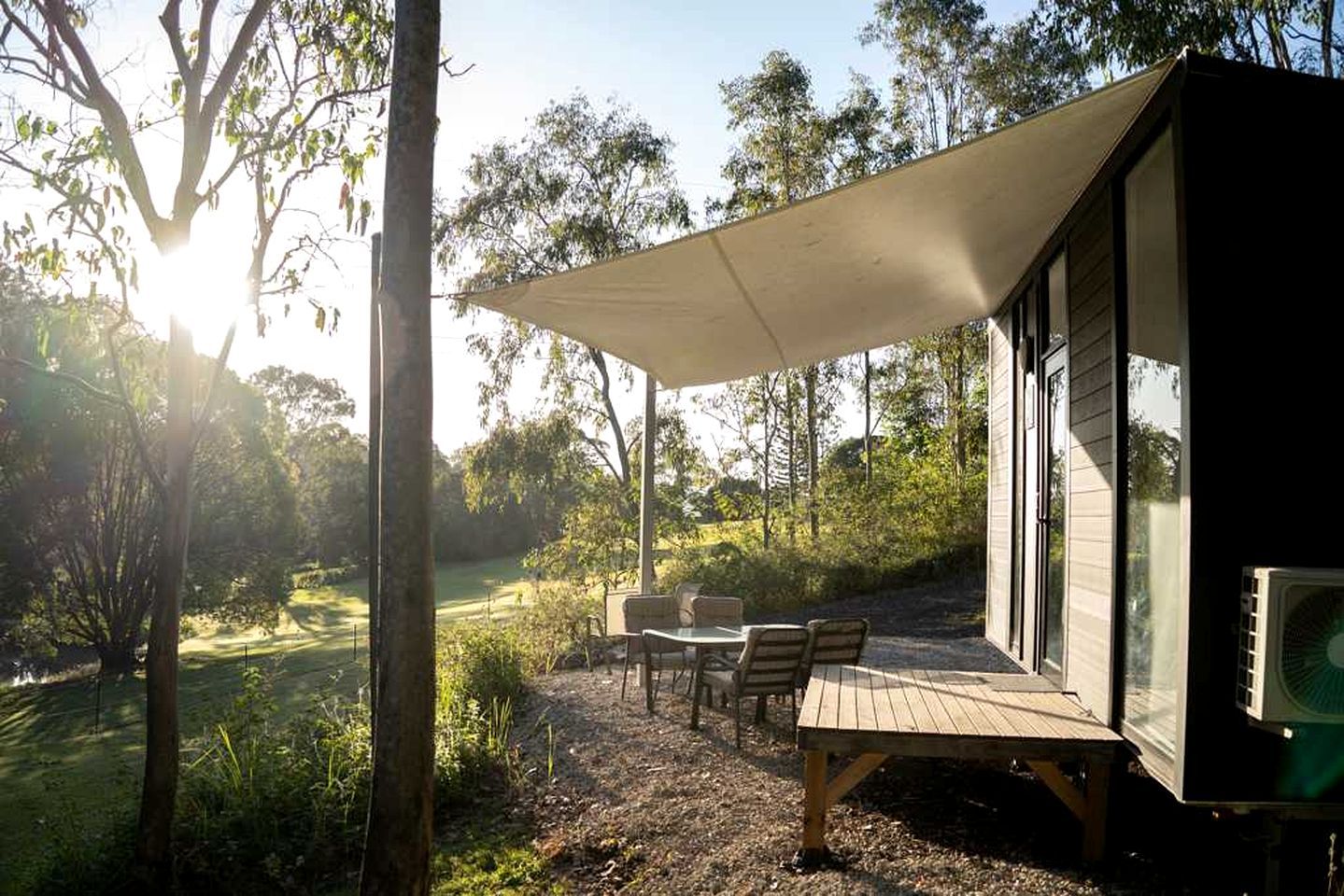 Un espace extérieur abrité, avec une table et des chaises, entouré d’arbres et de végétation.