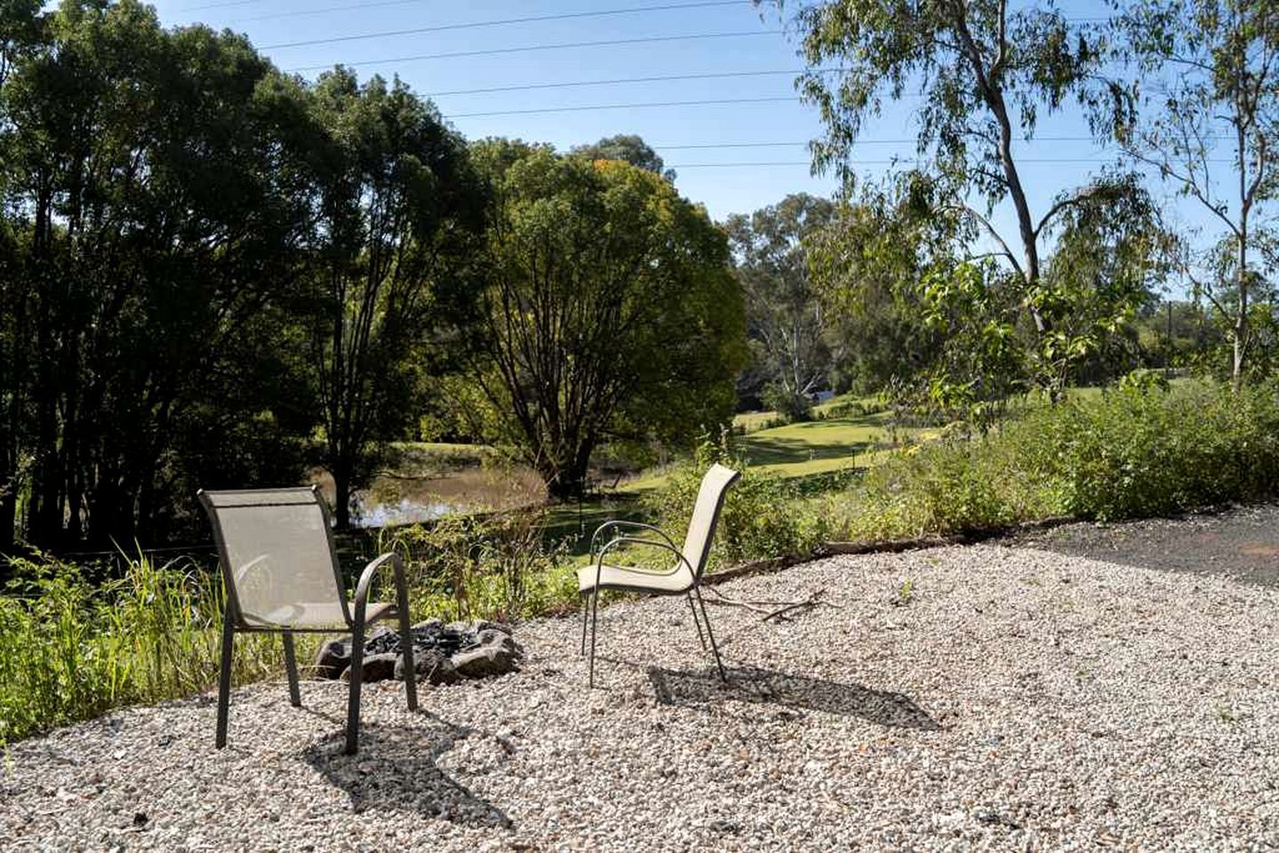 Two chairs and a table on a gravel surface with a view of a grassy area and trees.