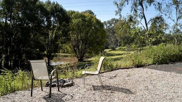 Two chairs and a table on a gravel surface with a view of a grassy area and trees.