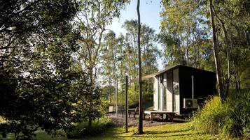 A cabin in a forested area with a clear view of the surrounding trees and a bench outside.