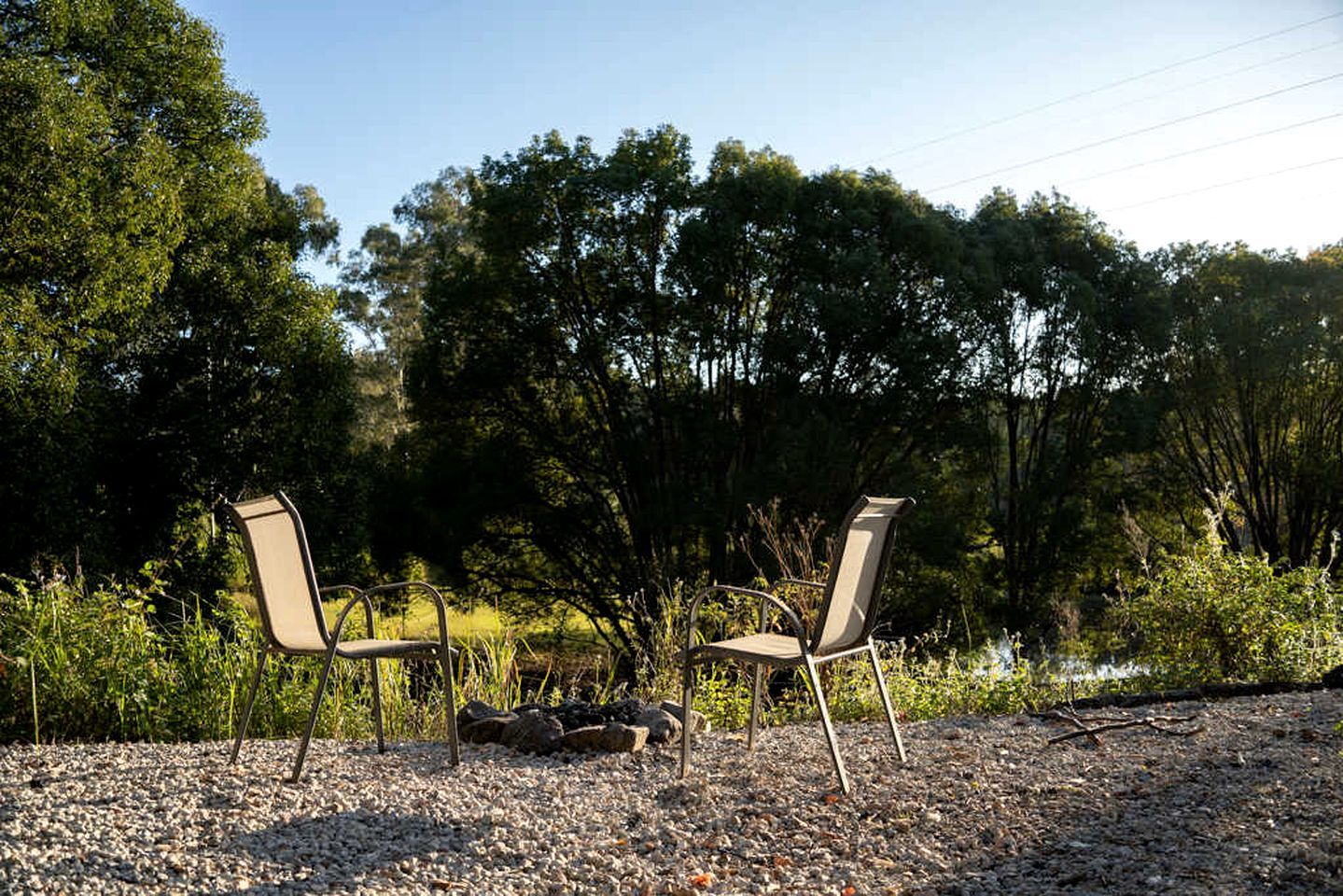 Two chairs positioned on a gravel surface with a natural backdrop of trees and foliage.