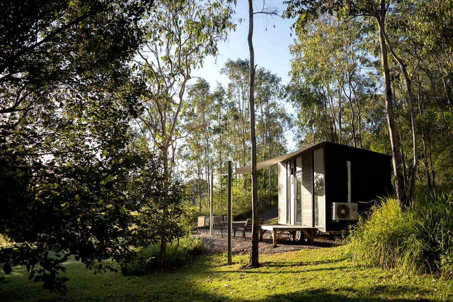 Une cabane située dans une zone boisée, offrant une vue dégagée sur les arbres environnants, avec un banc à l’extérieur.