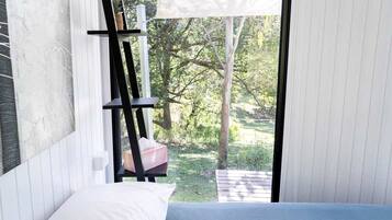 A bedroom with a bed, a window, and a view of a garden.