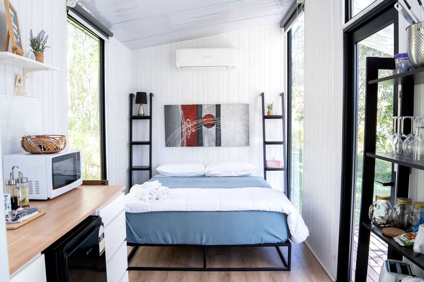 Een compacte slaapkamer met een bed, een kleine kitchenette en een groot raam voor natuurlijk licht.
