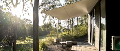 A covered outdoor seating area with a table and chairs, surrounded by trees and vegetation.
