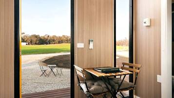 A room with a wooden interior, a table with chairs, a bench, and a view of a grassy area outside.