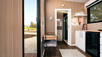 Cocina compacta con refrigerador integrado, un pequeño comedor con banco y vista al exterior.