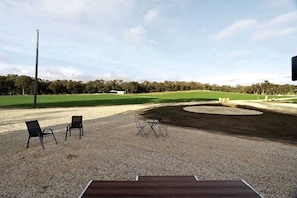 An outdoor seating area with chairs and tables, a gravel surface, and a view of a golf course.
