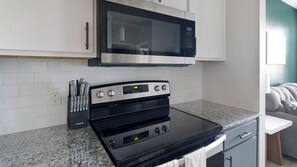 Una cocina con microondas de acero inoxidable, horno negro y encimera de granito.