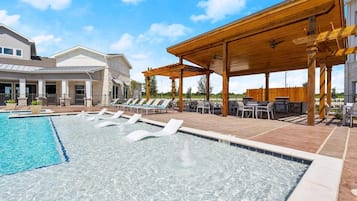 A swimming pool with lounge chairs, a covered patio area, and a building with a stone facade.